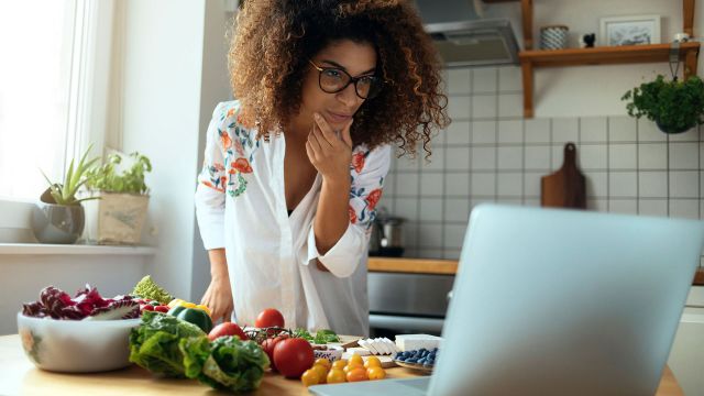 Woman chopping vegetables while looking at a recipe on her laptop