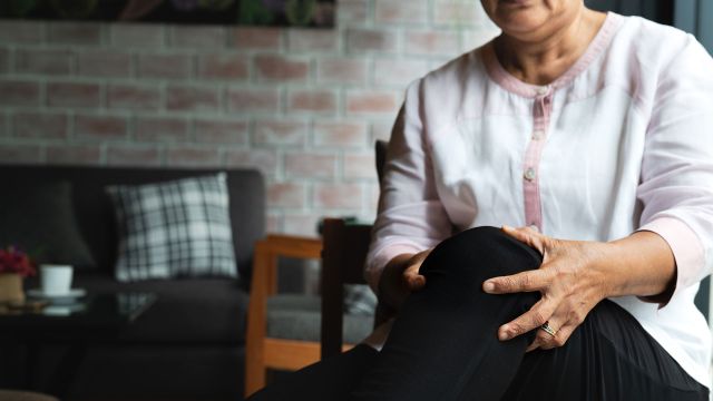 An older woman grips her knee in pain, wondering if knee support or a brace will help. 