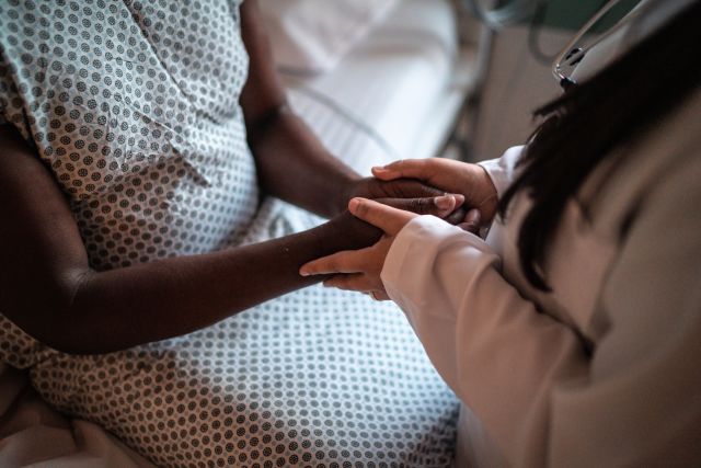 A doctor holds her patient’s hands as she explains her pancreatic cancer prognosis.  