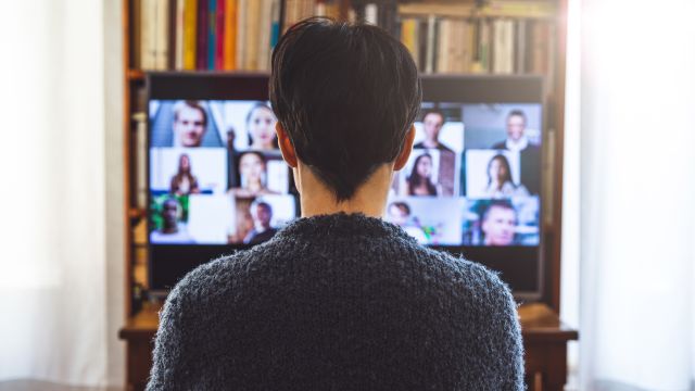 A woman sits in front of her computer while on a videoconference call with many participants.