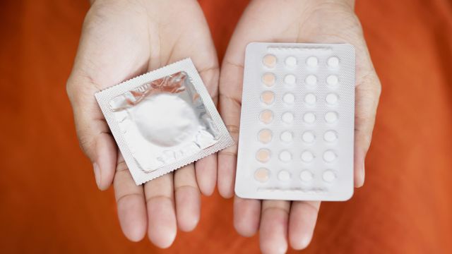 Woman holds birth control pills in one hand and a condom in the other.