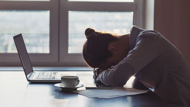 Exhausted woman has head down on desk at work.