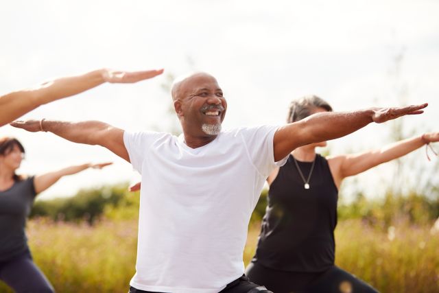 Middle-aged Black man does yoga stretch outdoors with other exercisers 