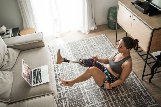 person with artificial lower limb exercising at home while watching a laptop