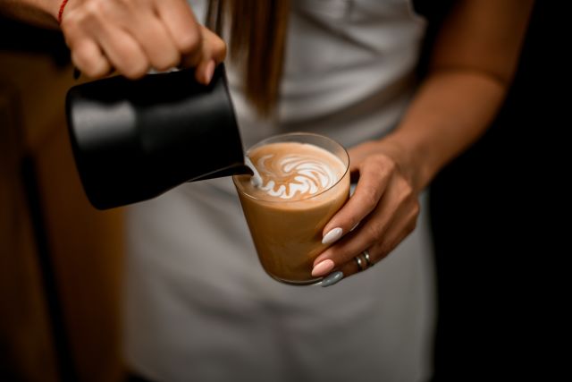 a barista pours milk into a latte coffee drink