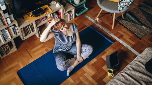Woman sitting cross legged on a yoga mat and stretching to manage stress and get endometriosis pain relief 