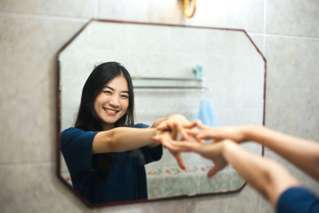 a young Asian woman looks in the mirror and conveys positive thoughts to herself