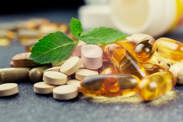 An array of dietary supplements and herbal remedies are laid out on a kitchen counter.