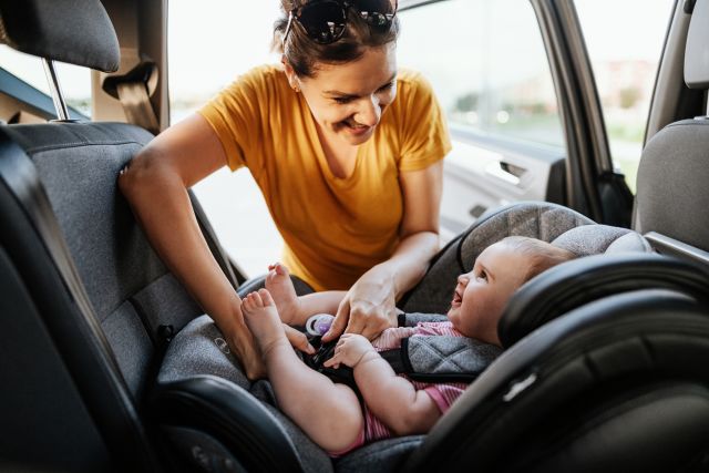 a woman buckles a baby into a child car seat