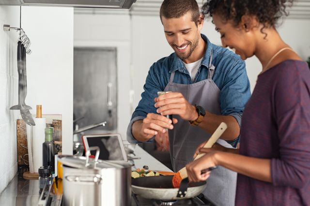 a young, happy mixed race couple prepares a meal in the kitchen, using freshly ground pepper as a seasoning in place of salt