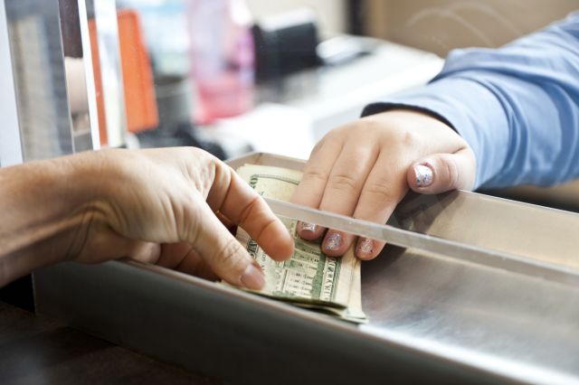a bank teller pushes several dollar bills through the slot at a bank to a customer