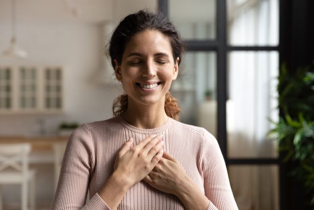 a middle aged Hispanic woman smiles with eyes closed, resting her hands gently over her heart