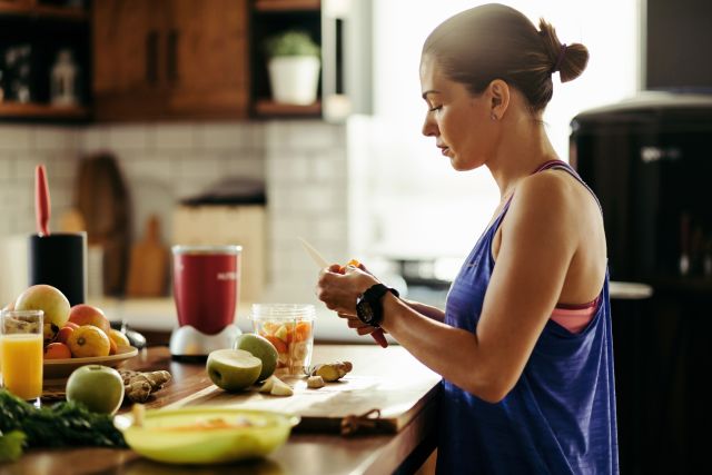 A middle-aged white woman in workout wear prepares a fruit smoothie in her kitchen