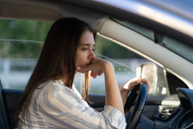 A tired young white woman sits in her car struggling to stay awake