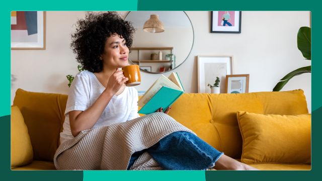 Woman with PsA sits on couch with drink.