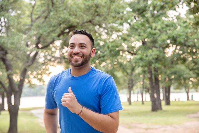 a young man with a beard wearing fitness gear smiles as he goes for a walk in the park