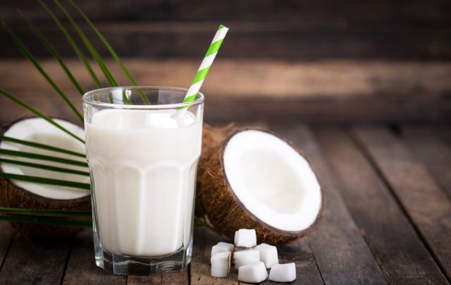 a glass of coconut milk with a straw next to a split coconut