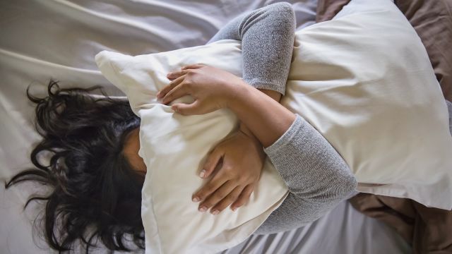 Young woman holds pillow over face.