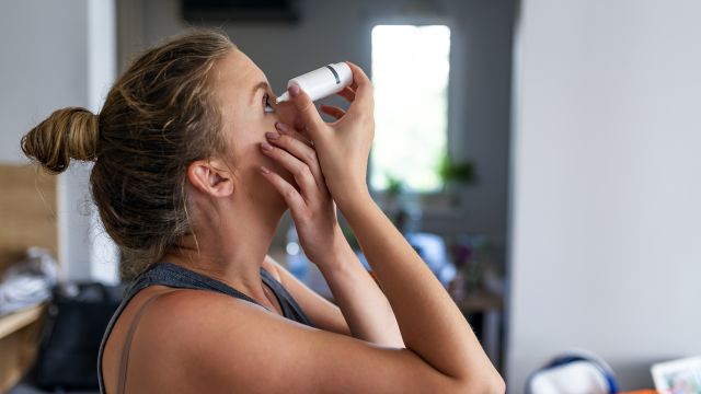 A woman uses eye drops. Liquid teardrops are a common treatment for thyroid eye disease.