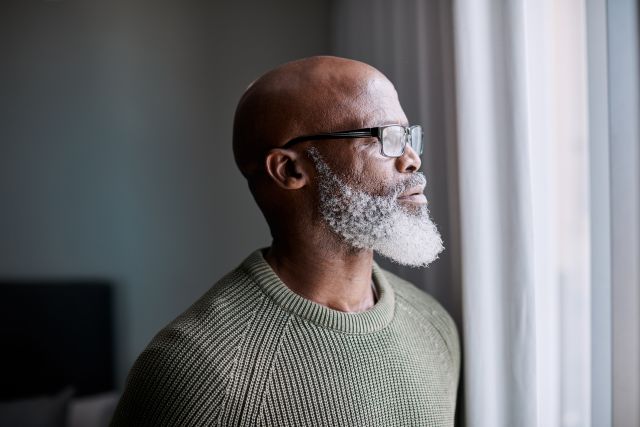 a middle aged Black man with a shaved head, glasses, and a gray beard gazes thoughtfully out a window