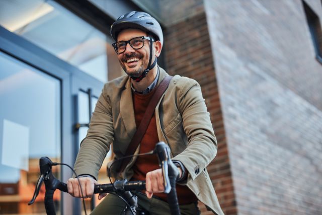 smiling man wearing helmet riding bike to work