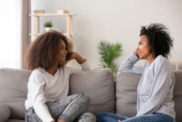 African American mother sitting on couch with teen daughter chatting about adhd