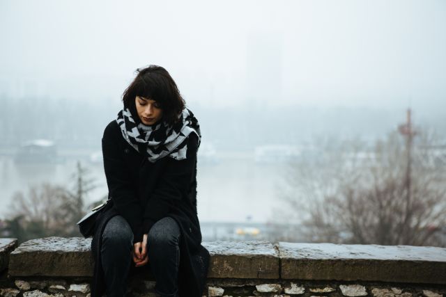 sad woman with bipolar disorder sitting alone on a bench in front of a lake