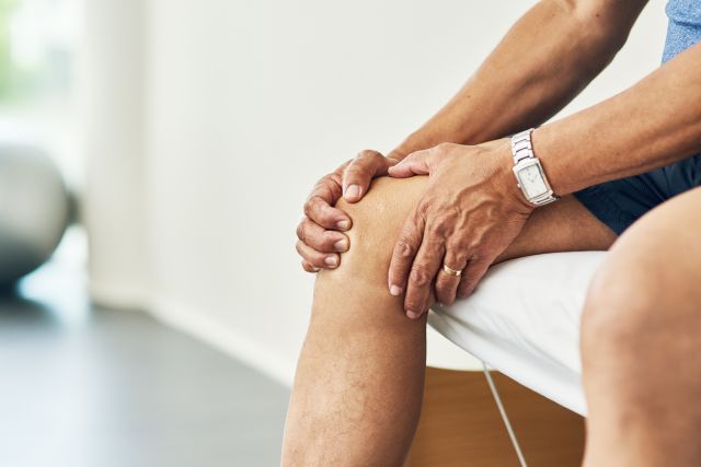 Cropped shot of an unrecognizable person sitting on a bed holding his painful knee