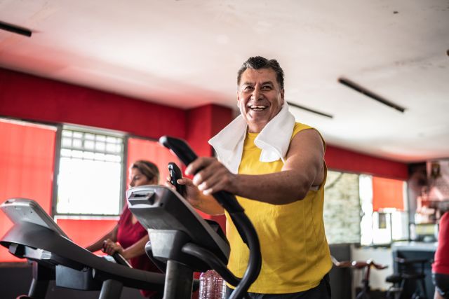 Smiling senior Man exercising on elliptical at gym