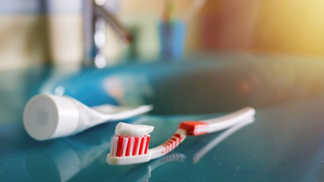 A toothbrush and toothpaste wait on a sink.