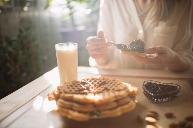 view of woman spreading blackberry jam onto her waffles in the morning light of her breakfast table