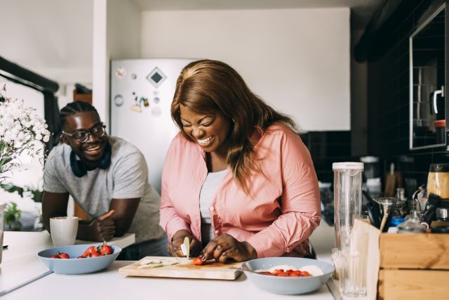 laughing couple in kitchen preparing a healthy meal together