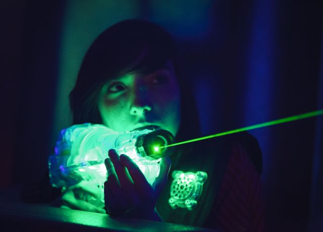 A teen girl holding up a laser tag gun, laser shooting from toy gun