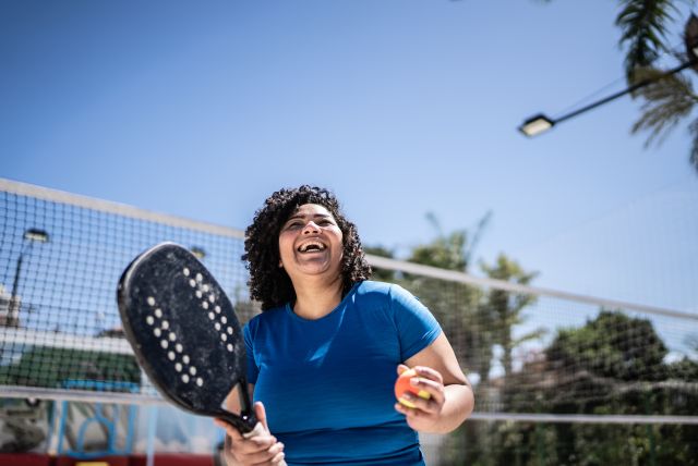 View of a woman smiling holding a beach tennis racket and ball