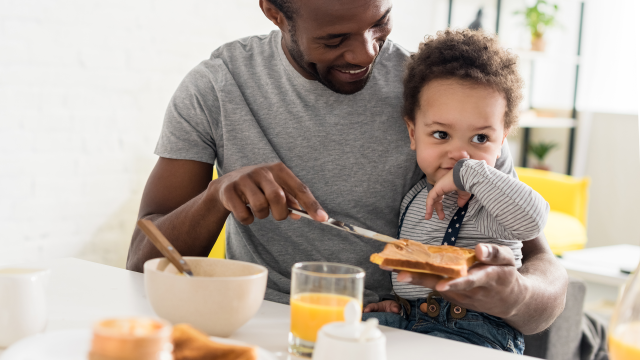 father applying peanut butter on toast for a baby boy