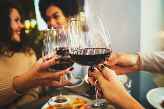 happy friends clinking red wine glasses at restaurant