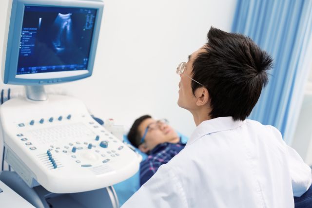 A urologist performing an ultrasound on a male patient who lies back on an exam table