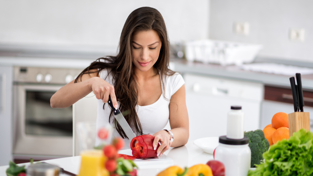 woman cutting up a bell pepper in her kitchen with broccoli, oranges and strawberries