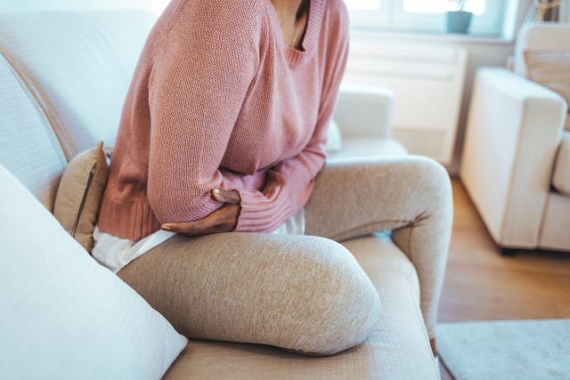 Woman sitting on a couch holding her stomach bent over in pain