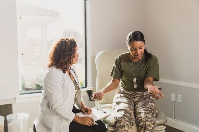 A concerned female veteran discusses psoriasis on her arms with a female dermatologist.