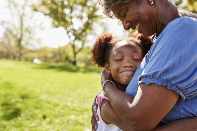 a Black grandmother hugs her smiling granddaughter