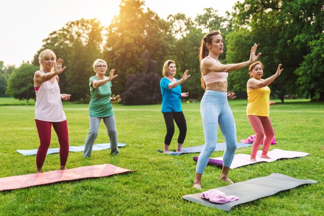 a group of women of various ages and ethnic backgrounds perform tai chi on a pleasant day in a park setting