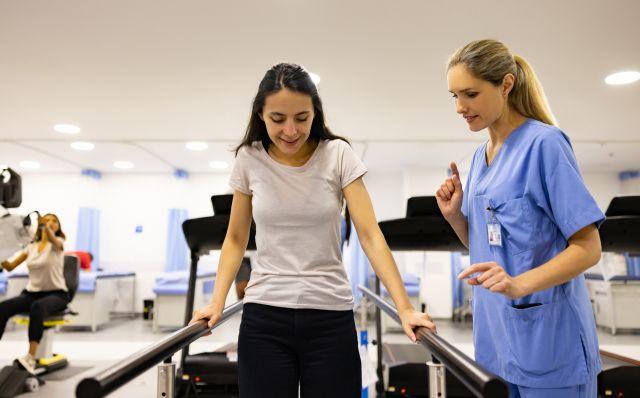 A young woman works with a physical therapist to improve balance while walking. Physical therapy is often a component of treatment for FRDA.