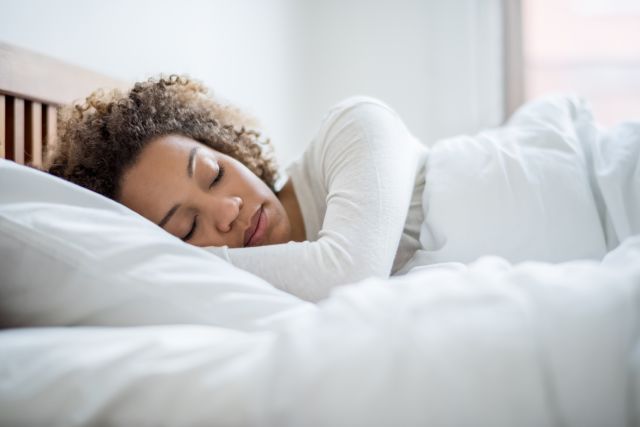 a young Black woman sleep peacefully on a bed on her side, with her fact turned toward the camera