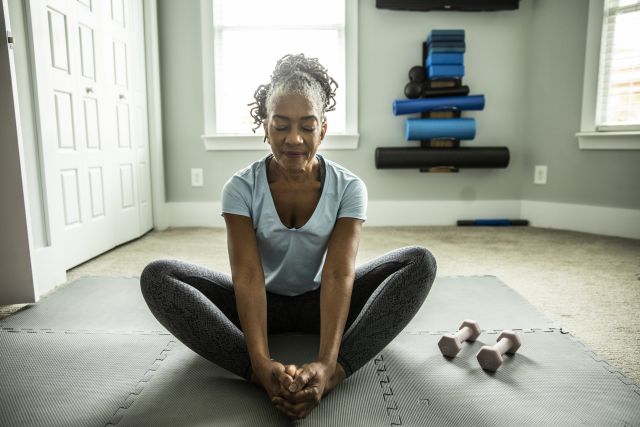 A senior woman practices yoga at home. Staying physical active is one of several strategies that can help a person stay healthy while living with AMD.