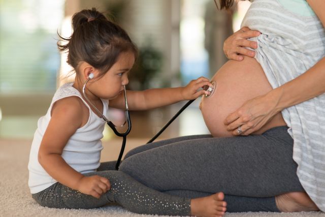 Toddler using a stethoscope to listen to the abdomen of a pregnant person