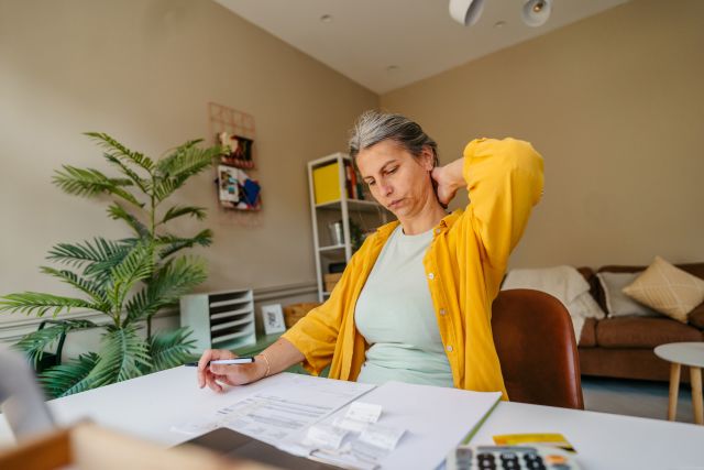 a middle aged white woman sits at her desk, paying bills and balancing her checkbook