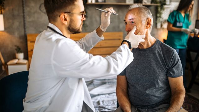 An ophthalmologist examines a senior man's eye with a flashlight as he prepares to administer an injection of medication into the eye.