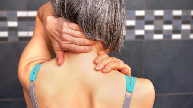 A woman massages her own shoulders to help alleviate neck pain.