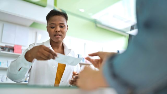 A customer hands a pharmacist a prescription for a psoriatic arthritis therapy.